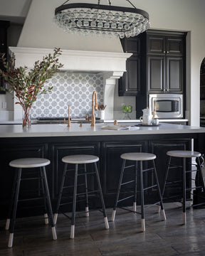 LOSTINE WHITEWASH GORDON STOOL - IRON BASE at kitchen counter under large chandelier- Classic ladder metal base stool with wooden seat and feet, workshop stool. Counter and bar height. Made by Lostine in Philadelphia. Simple interior design, made in the USA. Warm American Modern Design